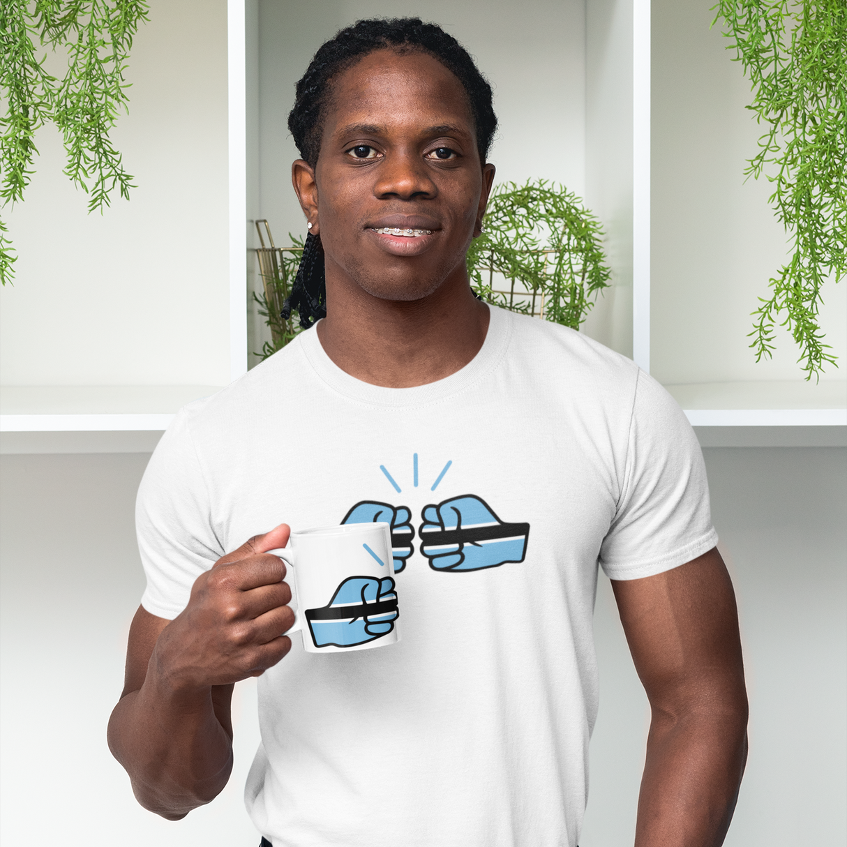 Man wearing a white t-shirt carrying a coffe mug with the We Run Tings Botswana design, standing in front of a white shelf with green plants.