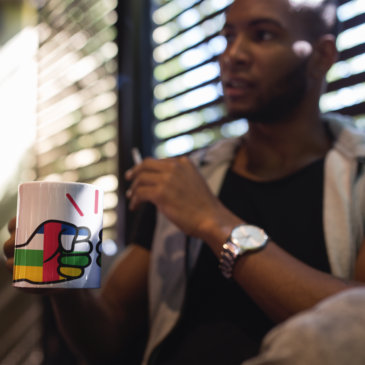 Man wearing a watch holding a We Run Tings Central African Republic (CAR) Mug
with a colorful design, blurred background
