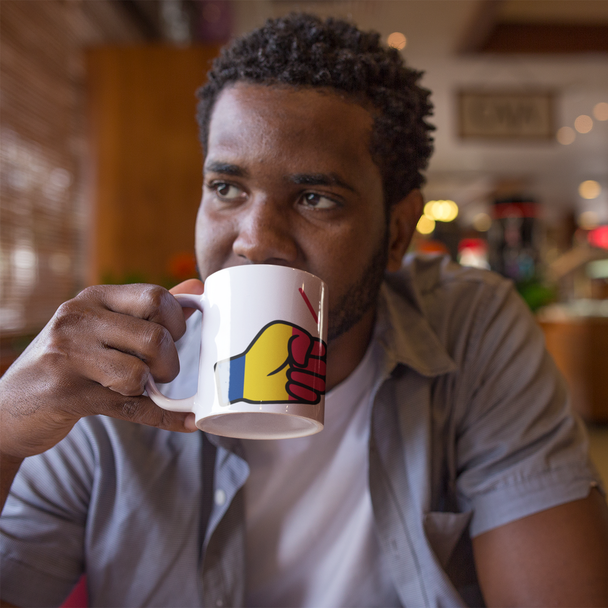 Man drinking from a We Run Tings coffee mug displaying a flag of Chad with in a blurred indoor setting