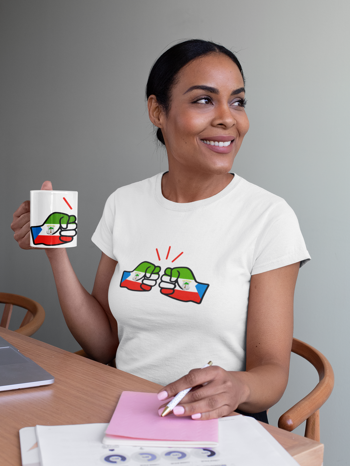 Woman wearing a white t-shirt with a We Run Tings Equatorial Guinea logo and holding a matching ceramic mug, and sitting at a table.