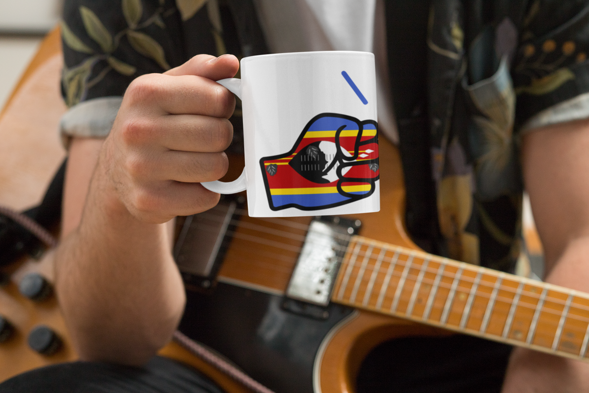 Person holding a Glossy white ceramic mug featuring a patriotic We Run Tings logo with two fists displaying the flag of Eswatini in front of an acoustic guitar