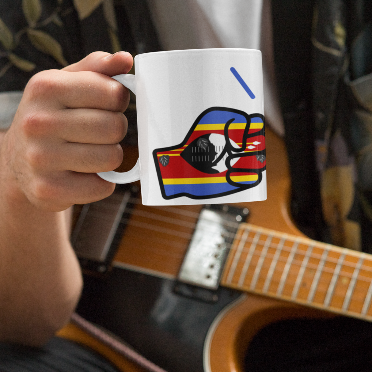 Person holding a Glossy white ceramic mug featuring a patriotic We Run Tings logo with two fists displaying the flag of Eswatini in front of an acoustic guitar
