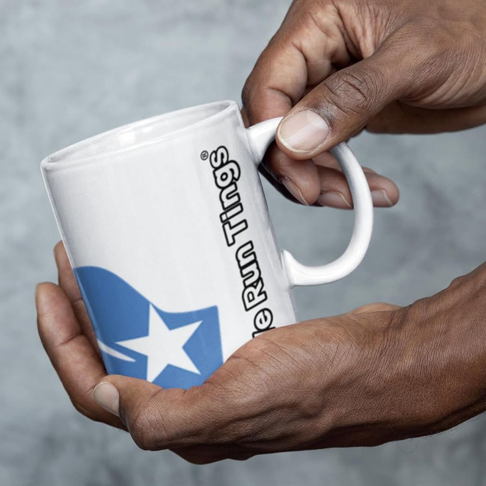 African person holding a white ceramic We Run Tings mug with flag of Somalia and text saying We Run Tings on a gray background
