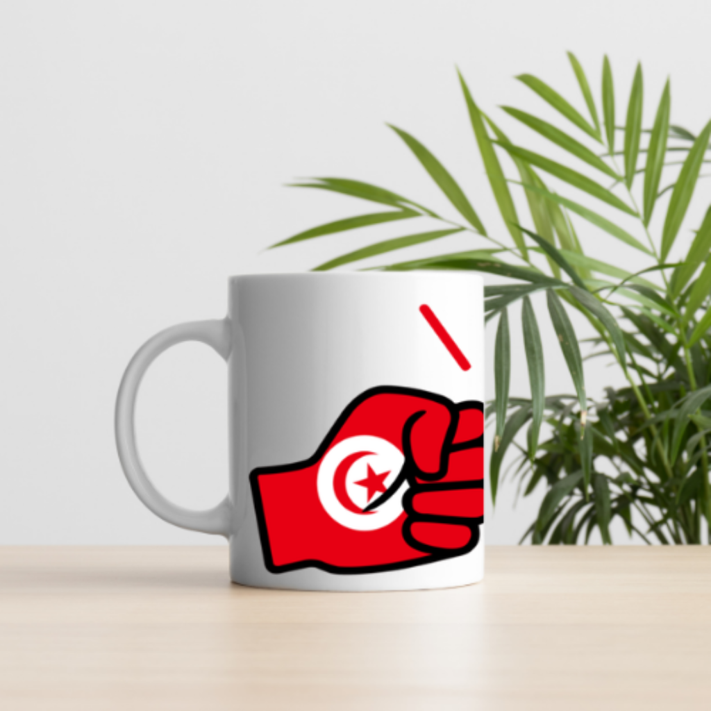 White mug with a red fist holding a white circle featuring a star on a light gray background, with a plant in the background.