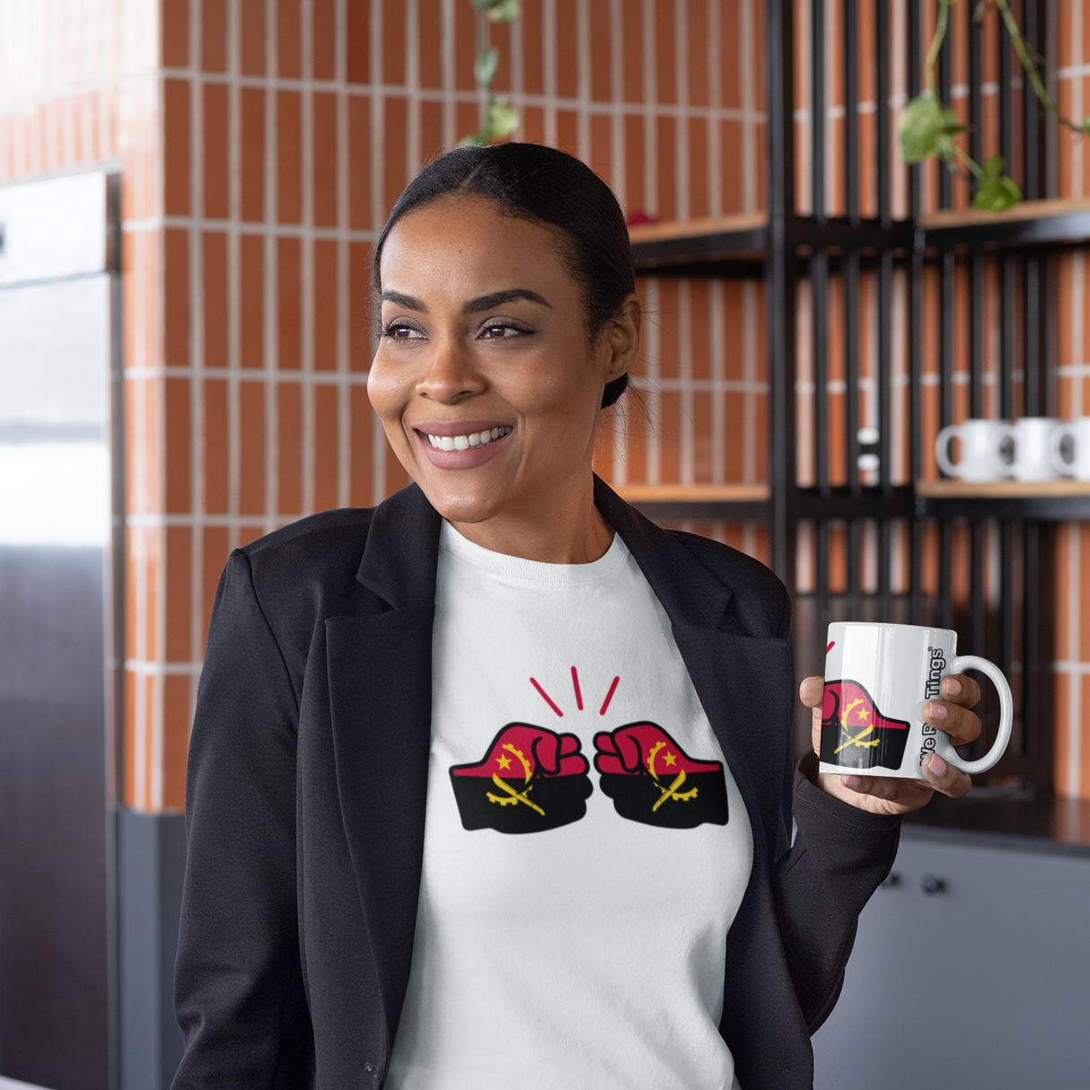 Woman holding a We Run Tings coffee mug displaying the flag of Angola in a kitchen wearing a white t-shirt with a graphic design and holding a mug.