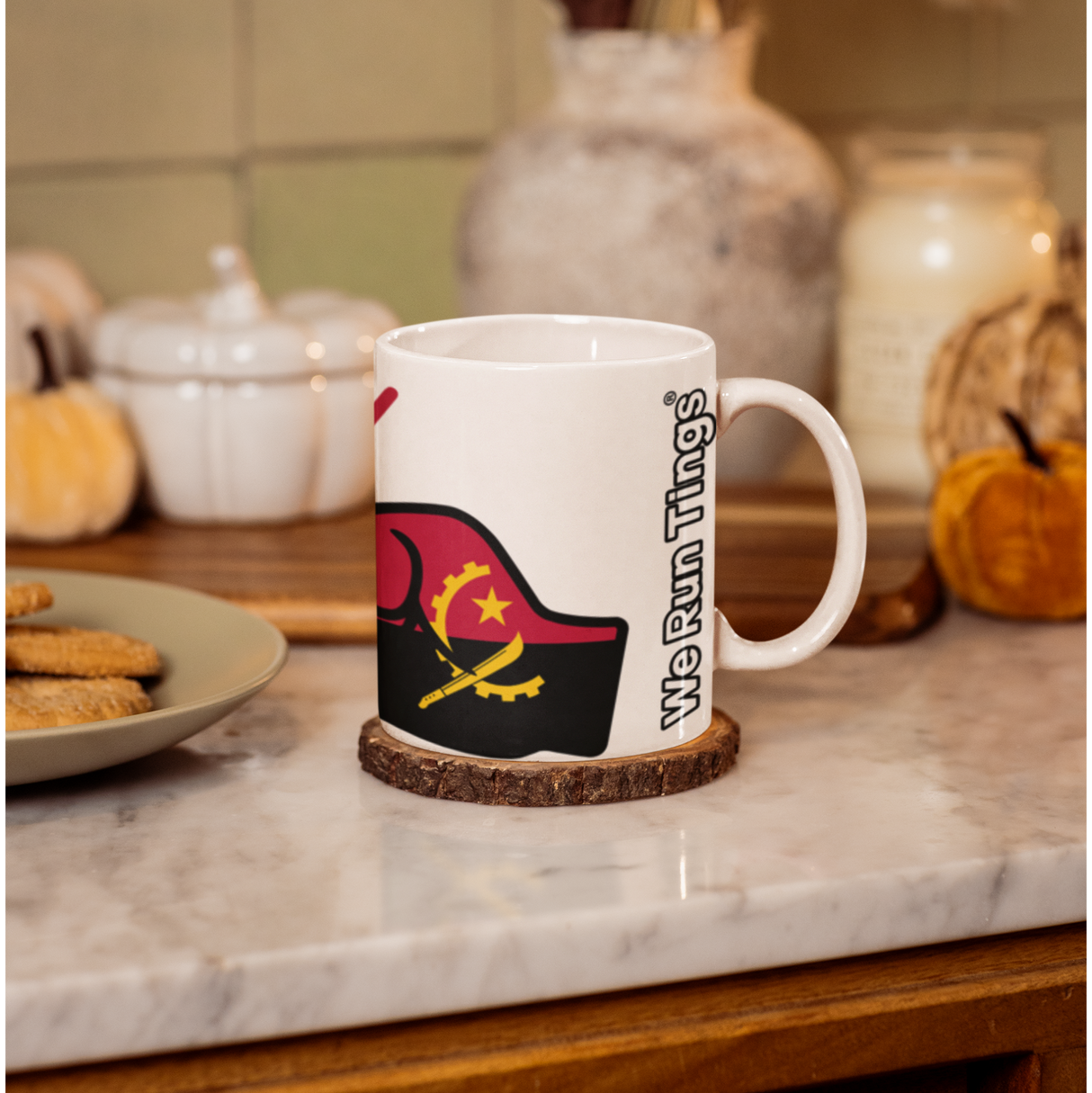 White coffee mug with a design of We Run Tings displaying the flag of Angola and text on a marble countertop with decorative items.