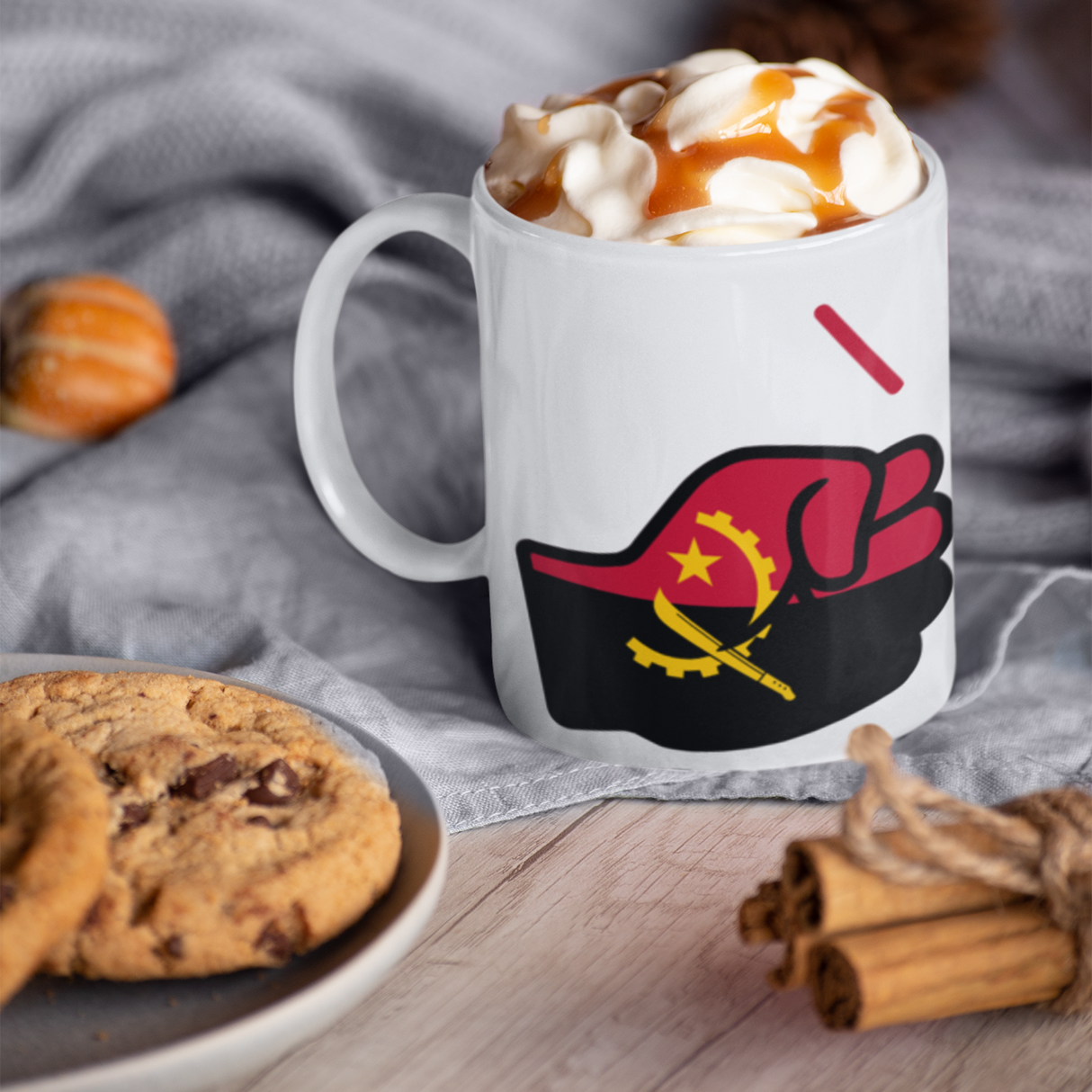 We Run Tings Coffee Mug with a design of a raised fist displaying a flag of Angola, surrounded by cookies and cinnamon sticks on a wooden surface.