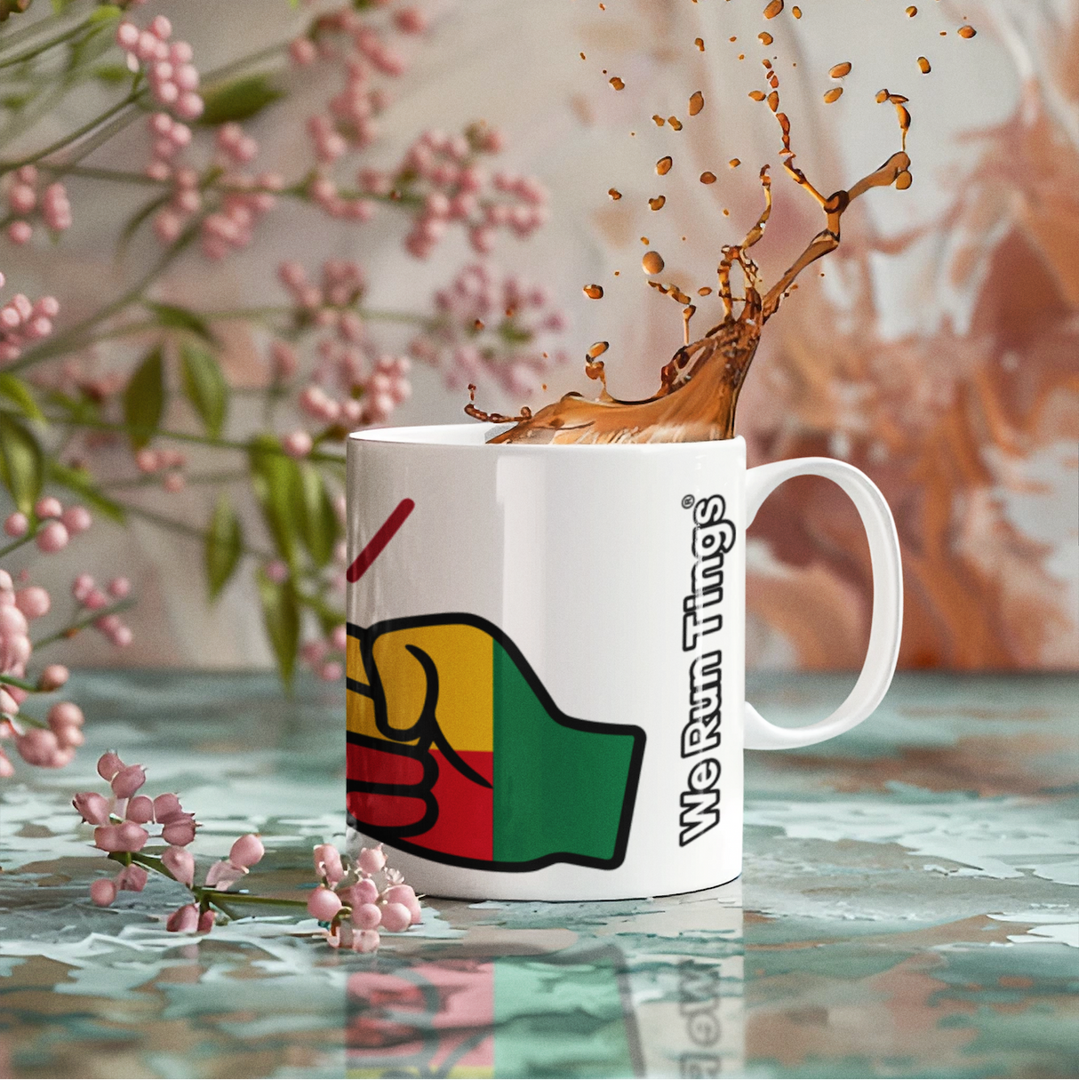 Mug with a raised fist logo and We Run Tings text and Benin flag filled with coffee, with pink flowers in the background.