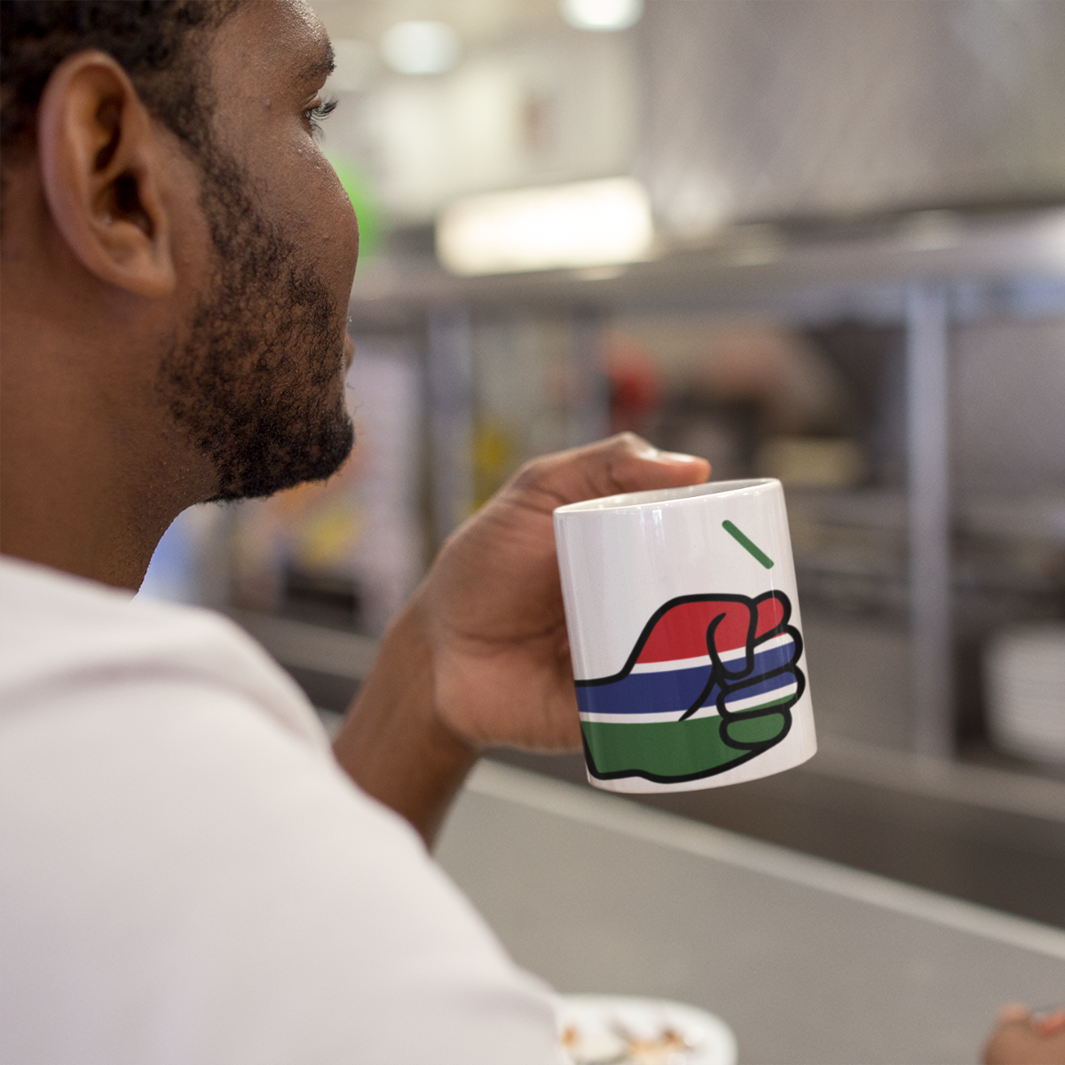 Man holding a We Run Tings Gambia mug with a colorful design in a coffee shop.