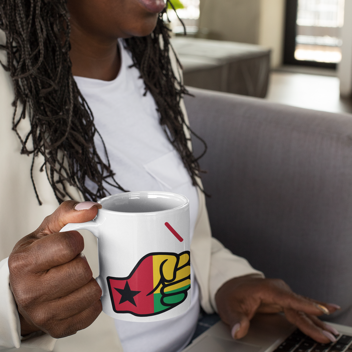 Woman holding a Guinea-Bissau themed We Run Tings mug with a colorful design, sitting on a couch using a laptop.