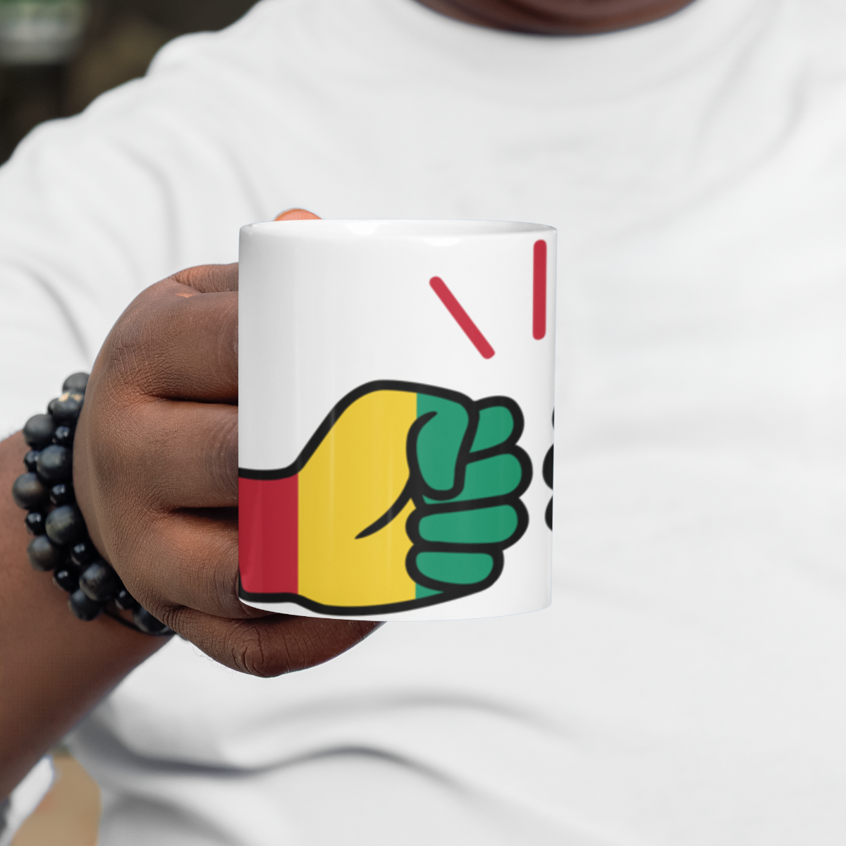 Person holding a We Run Tings Guinea mug with a raised fist design in red, yellow, and green.