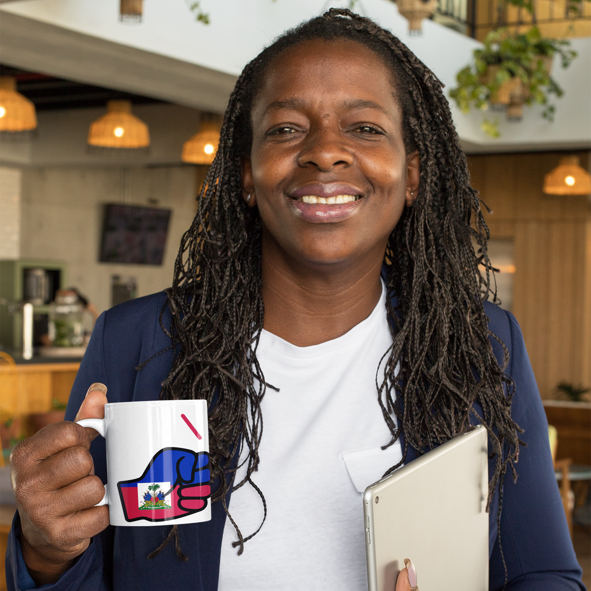 Woman holding a We Run Ting mug with a Haitian design and a tablet, standing in an indoor setting.