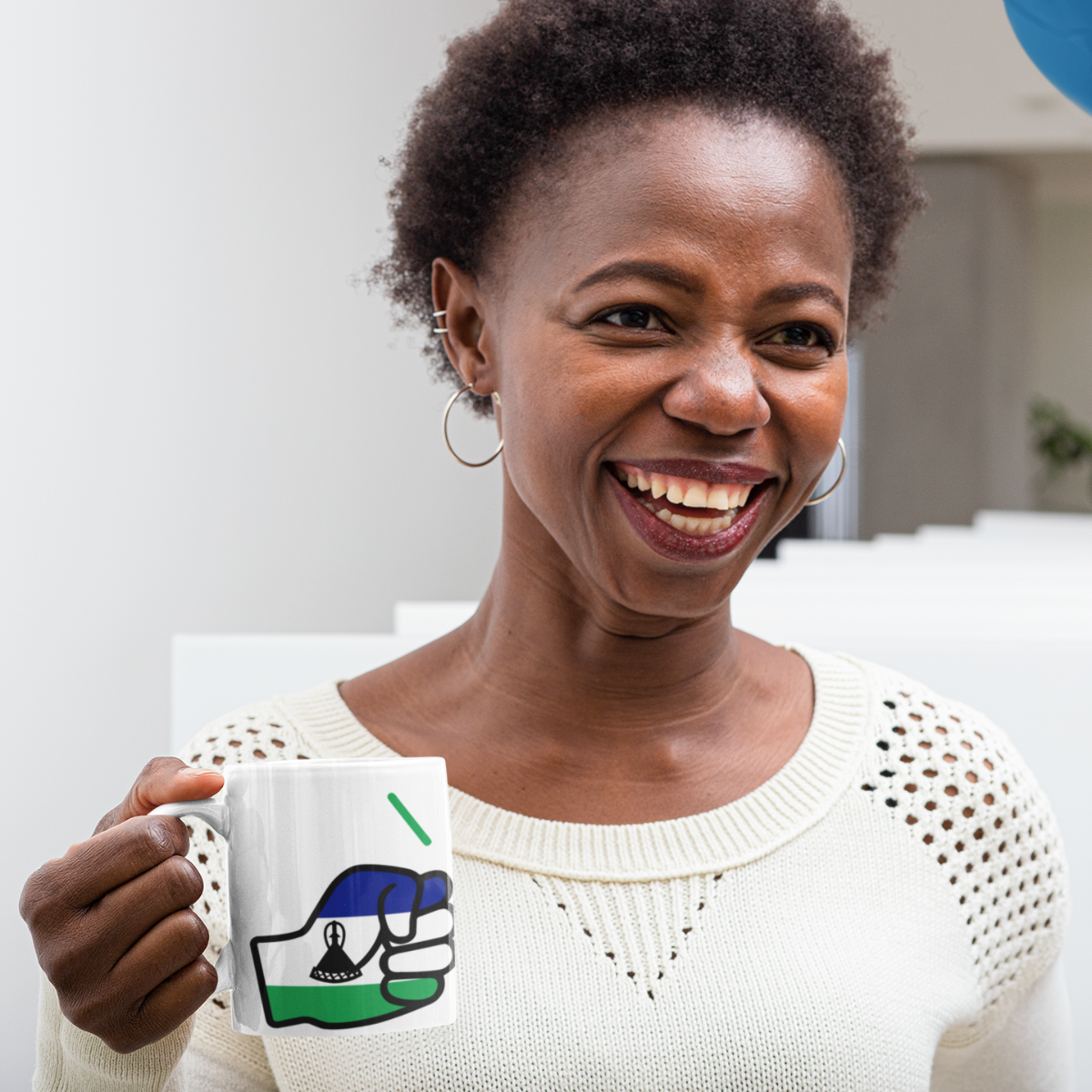 Woman holding a We Run Tings Lesotho white ceramic coffee mug with a design, smiling in a casual setting