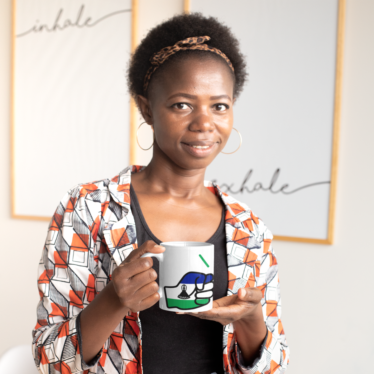 Woman holding a We Run Tings Lesotho white ceramic coffee mug with a colorful design in an indoor setting