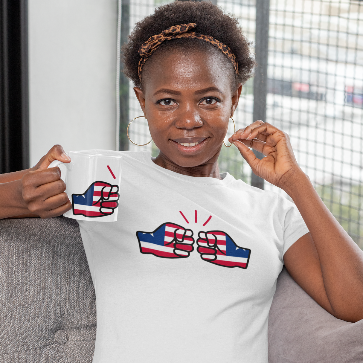 Woman wearing a white t-shirt with a graphic design, sitting on a couch holding a We Run Tings Liberia coffee Mug and matching t-shirt.