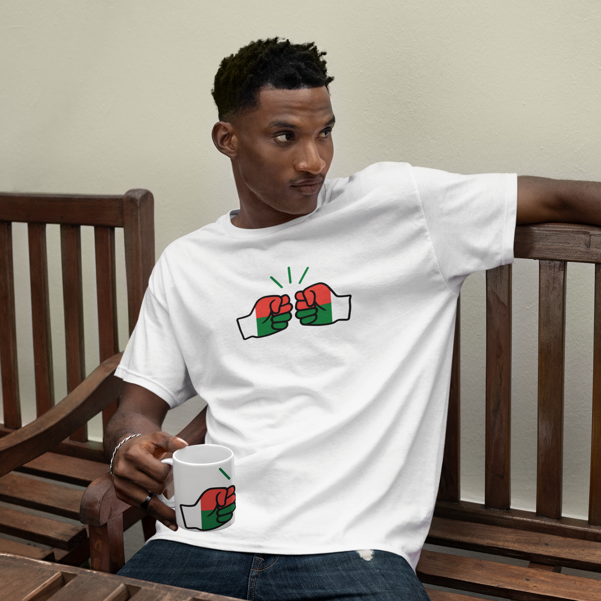 Man sitting on a wooden bench wearing a white t-shirt with a graphic design, holding a white ceramic We Run Tings Madagascar coffee mug.