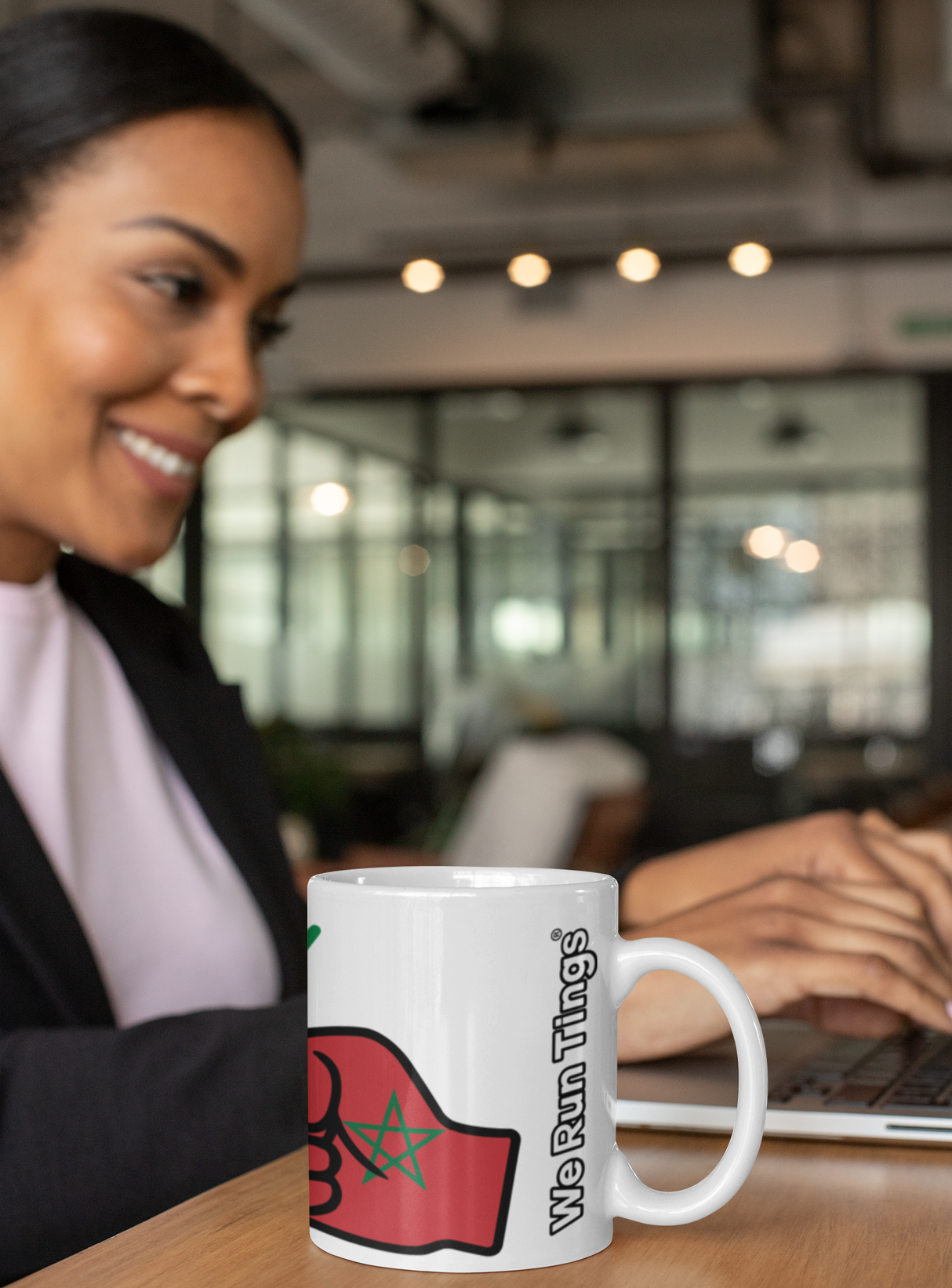 Woman in a professional setting with a white ceramic mug featuring a logo and text representing We Run Tings Morocco