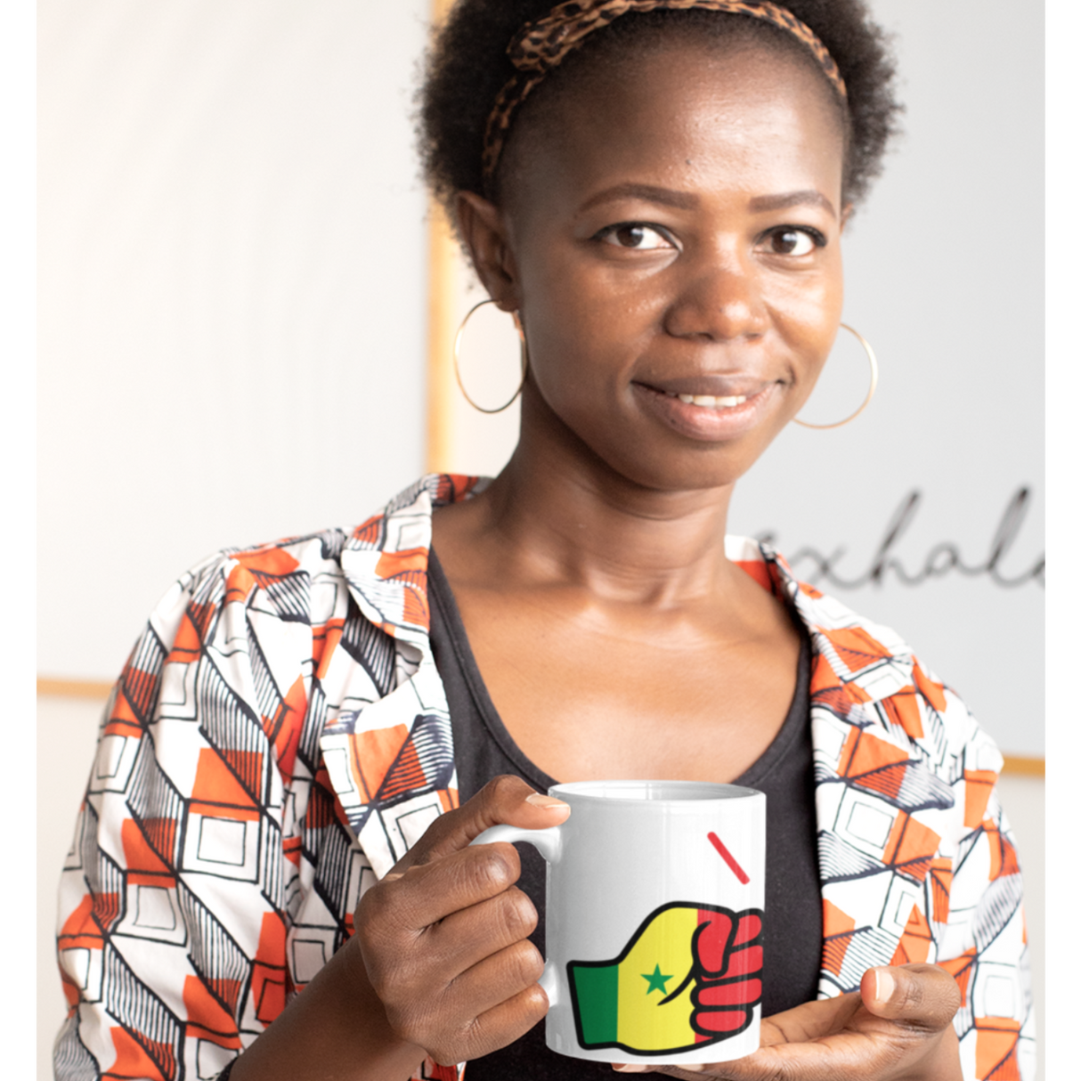 African Woman holding a We Run Tings Senegal themed mug with a colorful design, wearing an patterned shirt.