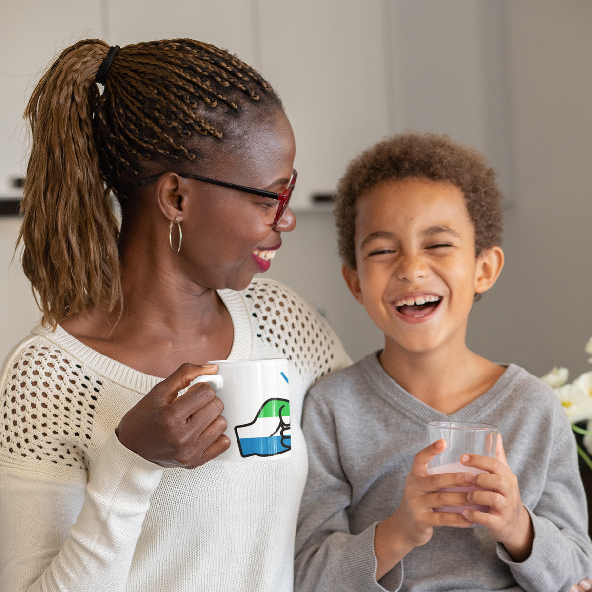 Woman and child sitting together smiling. Woman holding a Sierra Leone themed white ceramic coffee mug.
