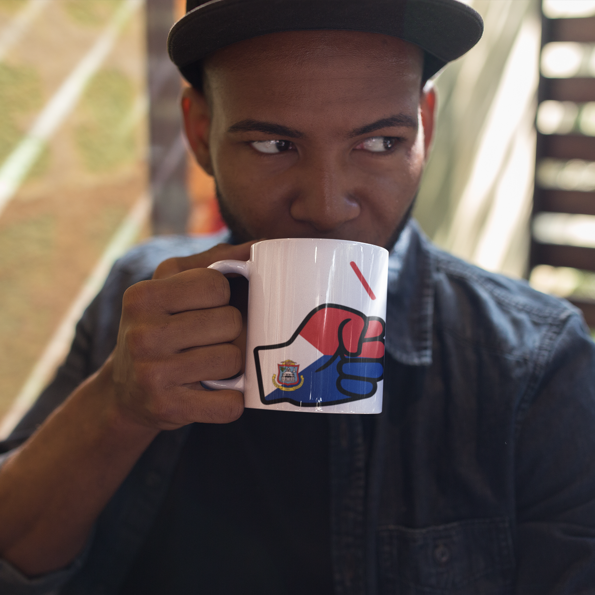 Man holding a mug with a graphic design of We Run Tings, St. Martin Mug wearing a denim shirt and cap.