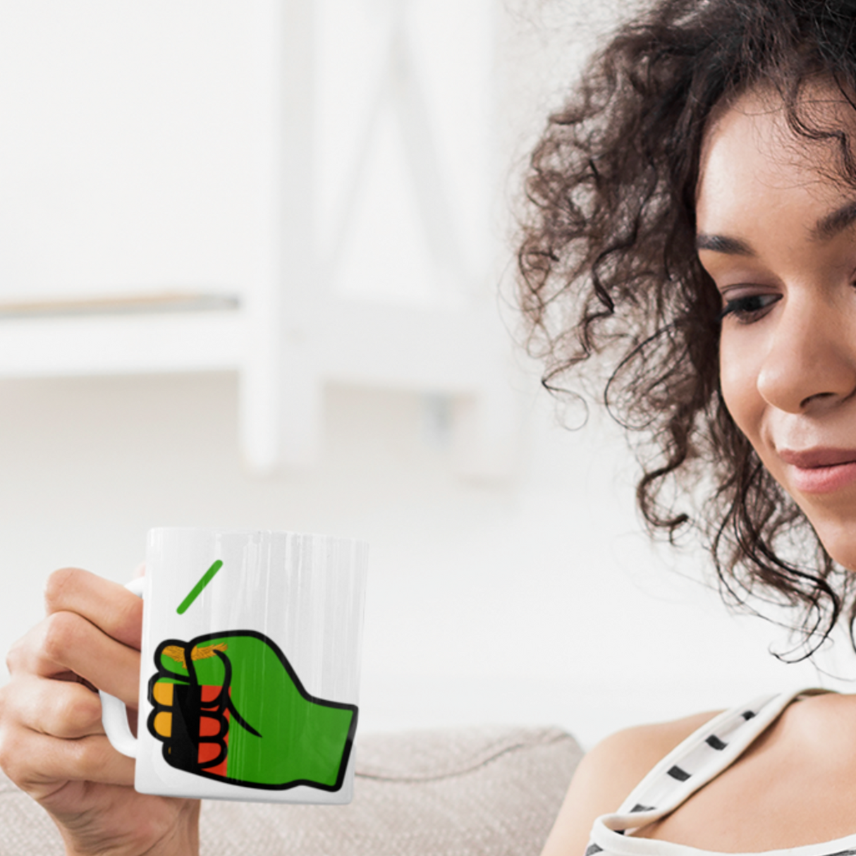 Woman holding a white glossy ceramic We Run Tings, Zambia themed mug featuring the brand logo, sitting on a couch.