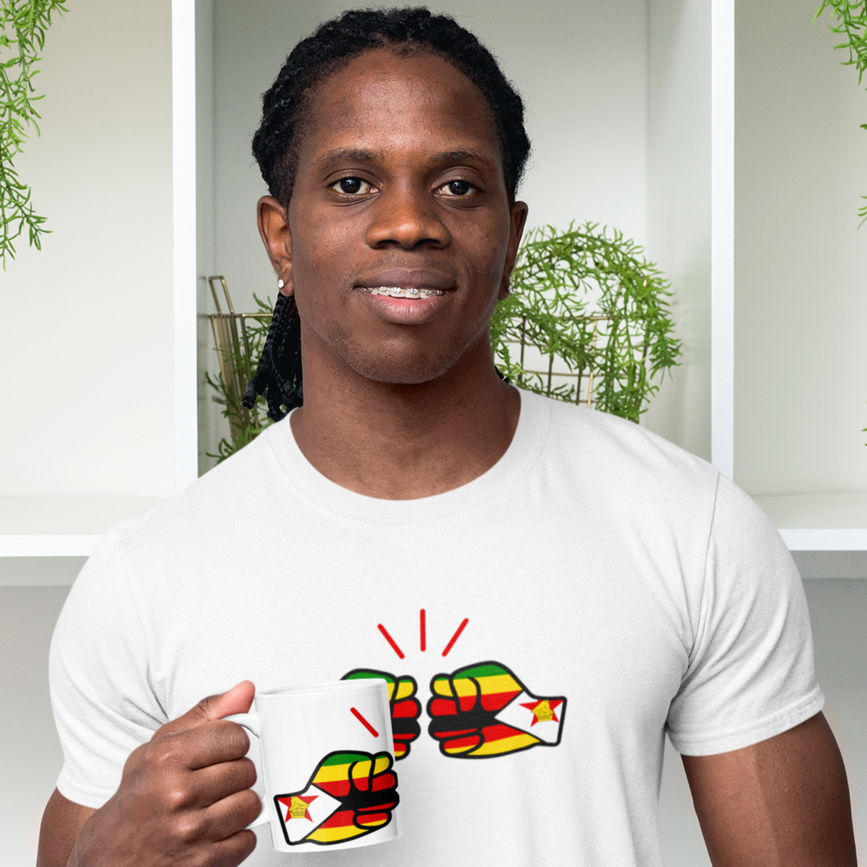 Black man smiling wearing a white We Run Tings, Zimbabwe themed t-shirt and matching white glossy ceramic mug with a colorful graphic design, standing indoors with plants in the background.
