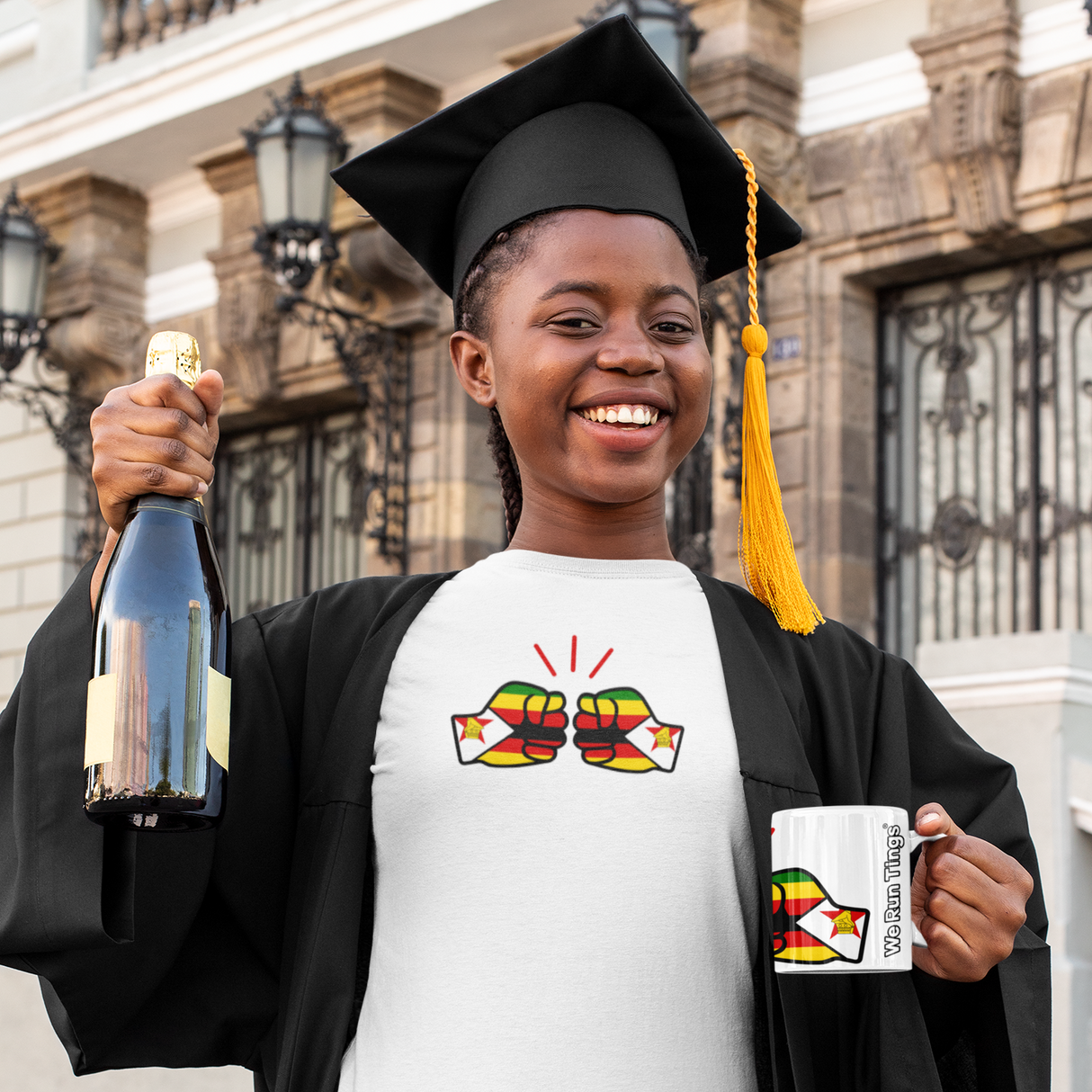 Graduate holding a bottle and white glossy ceramic tea, coffee We Run Tings, Zimbabwe theme mug whilst wearing a coordinating white t-shirt with a similar design.