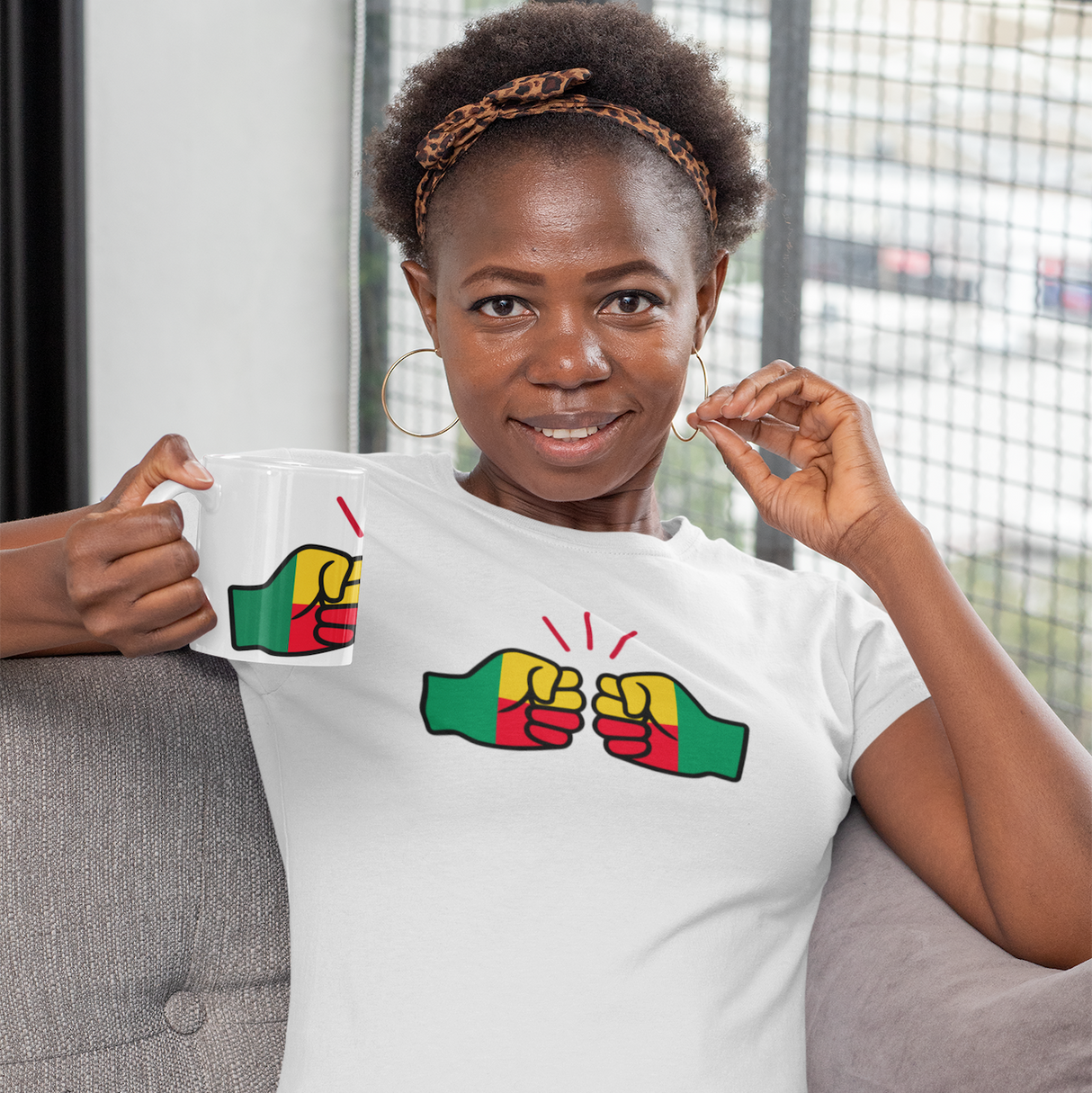 Woman wearing a white t-shirt with a We Run Tings logo and Benin flag colorful design, sitting on a couch.