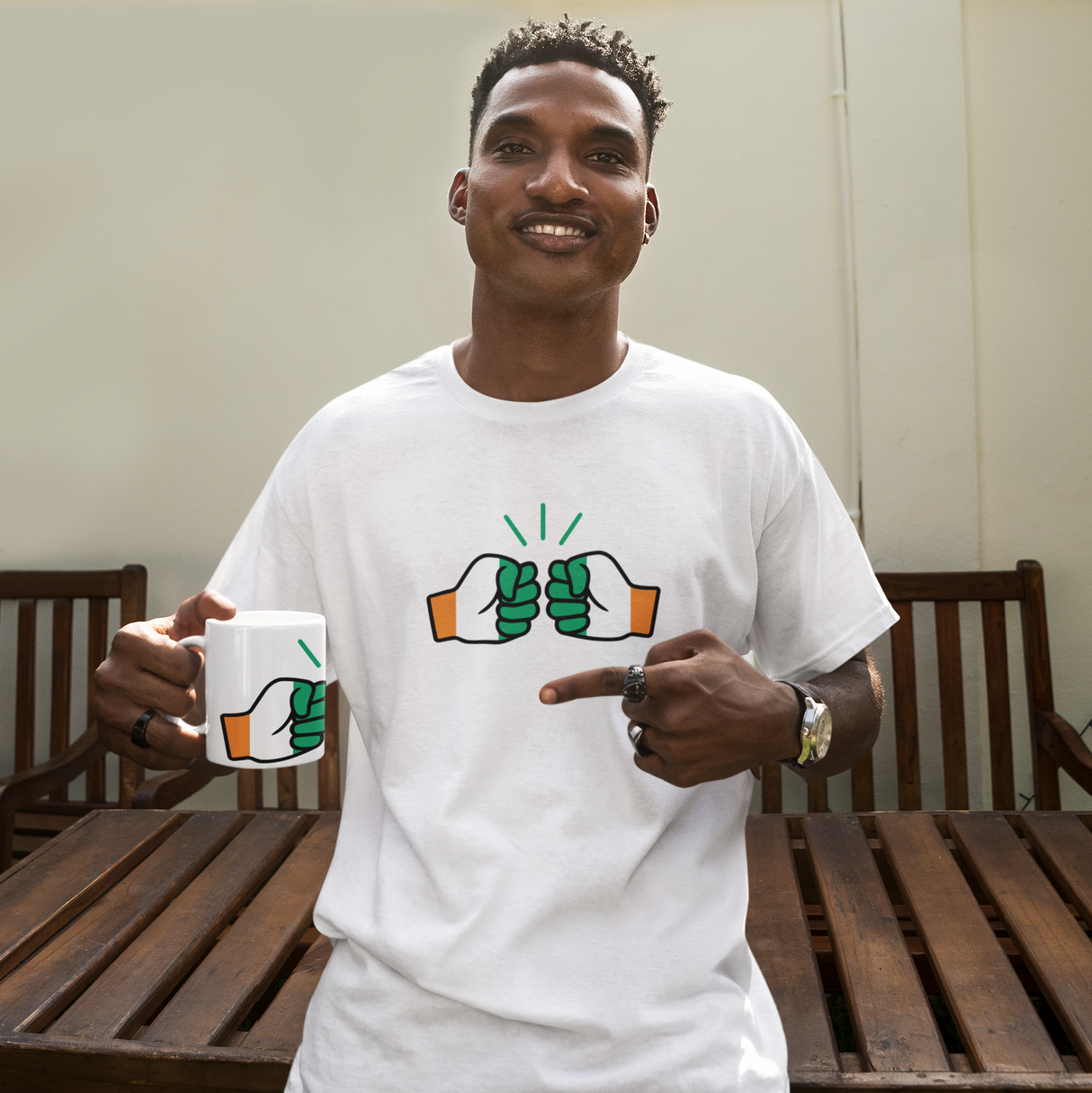 Man wearing a white Cote D'Ivoire t-shirt with a graphic design, holding a We Run Tings mug outdoors.