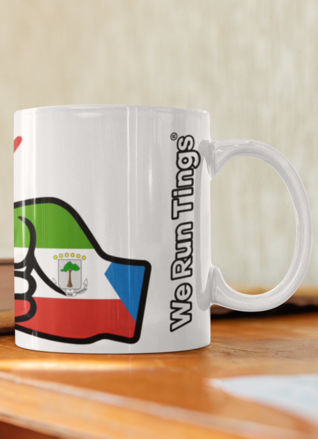 White ceramic We Run Tings Equatorial Guinea mug with colorful design on a wooden surface.