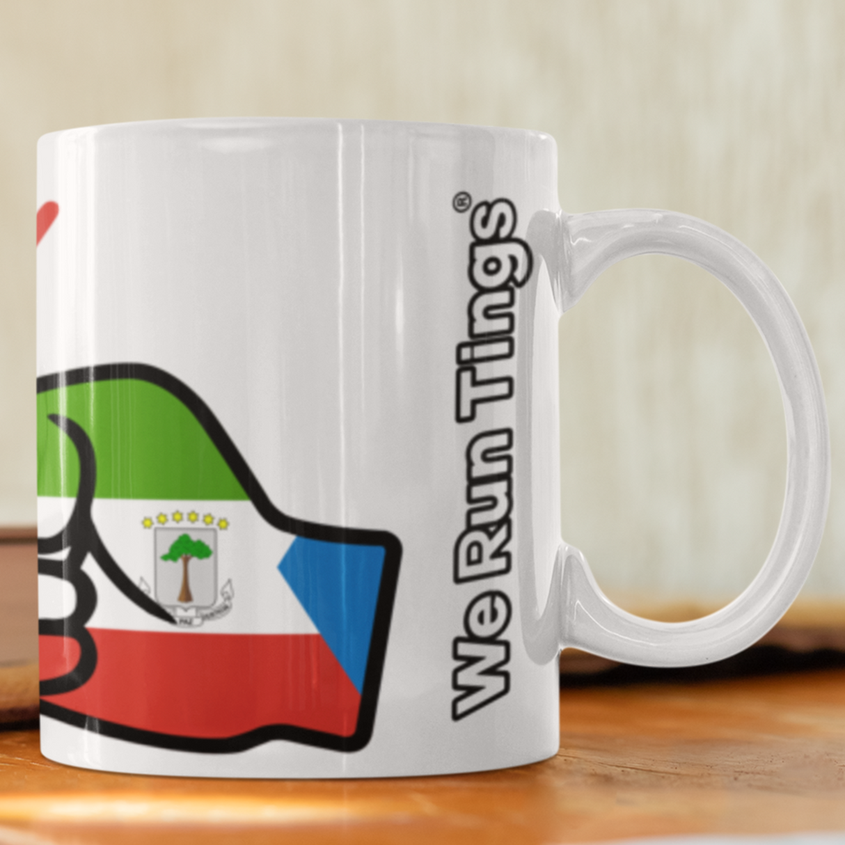 White ceramic We Run Tings Equatorial Guinea mug with colorful design on a wooden surface.