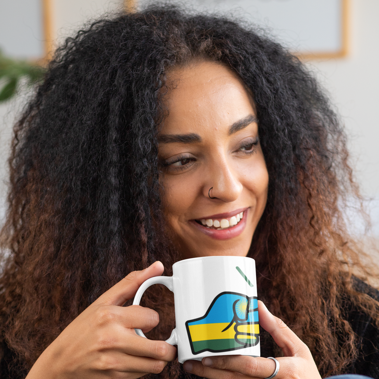 Woman smiling holding a white ceramic We Run Tings Rwanda tea, coffee mug, cup with a colorful design, sitting indoors.