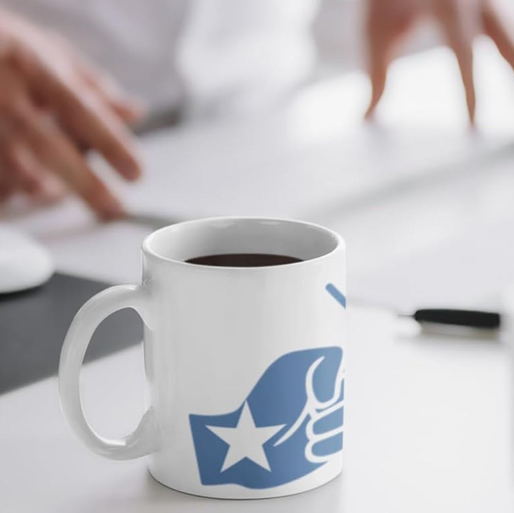 Black coffee in a white mug with the We Run Tings Somalia themed logo on a desk with a person using a computer in the background