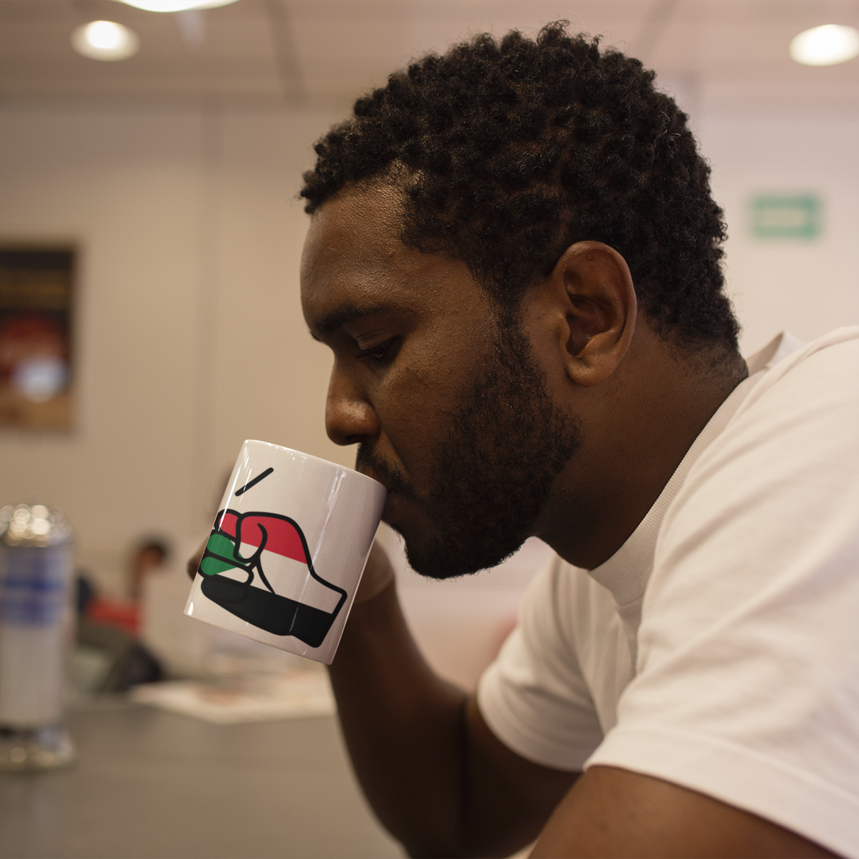 Man drinking from a white glossy ceramic Sudan themed We Run Tings tea, coffee mug in a casual setting
