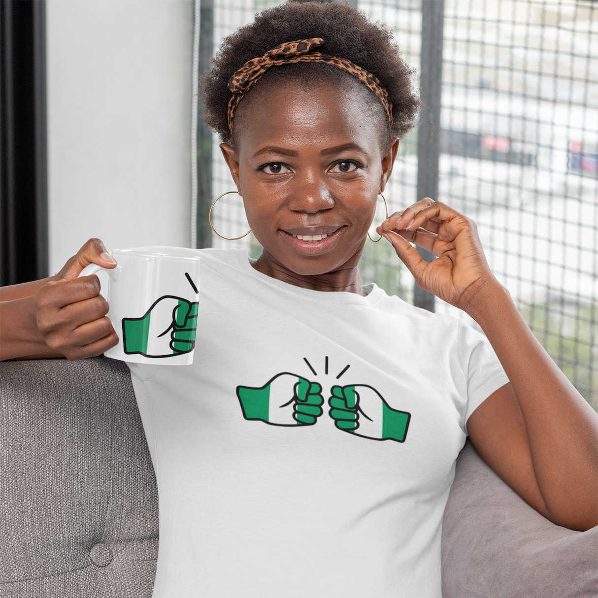 Woman holding a We Run Tings Nigerian themed white ceramic tea, coffee, mug, cup and matching branded t-shirt with a design on a couch