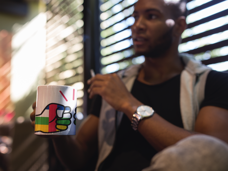 Man wearing a watch holding a We Run Tings Central African Republic (CAR) Mug
with a colorful design, blurred background
