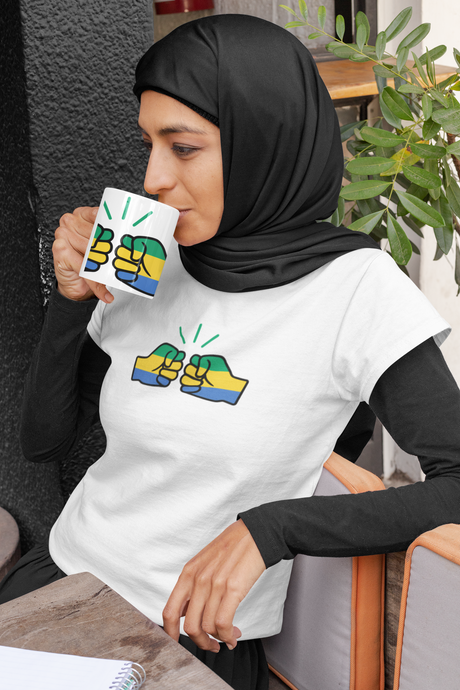 Woman wearing a hijab and white short sleeve t-shirt and holding a coffee mug both displaying the Gabon flag and We Run Tings brand logo