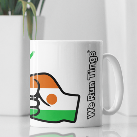 A glossy white ceramic We Run Tings Niger tea, coffee mug, cup with a graphic design of a fist and the colors of the flag of Niger. Side view with the words of the brand We Run Tings 