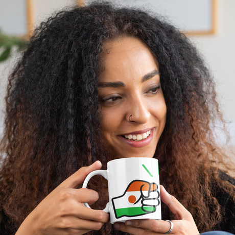 A curly haired woman holding a glossy white ceramic We Run Tings Niger tea, coffee mug, cup with a graphic design of a fist and the colors of the flag of Niger. Front view on a white background