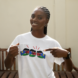 Woman smiling pointing to a white t-shirt with colorful graphic design of We Run Tings themed logo of South Sudan and matching white ceramic coffee, tea Mug