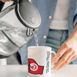 Person pouring water from a kettle into a mug with a visible brand logo of We Run Tings featuring the flag of Tunisia 
