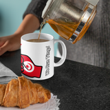 Person pouring tea from a glass teapot into a white mug with a We Run Tings logo, featuring the flag of Tunisia next to a croissant on a black surface.