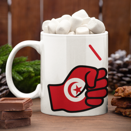 White mug with a We Run Tings Logo and flag of Tunisia design filled with hot chocolate and marshmallows on a wooden surface.