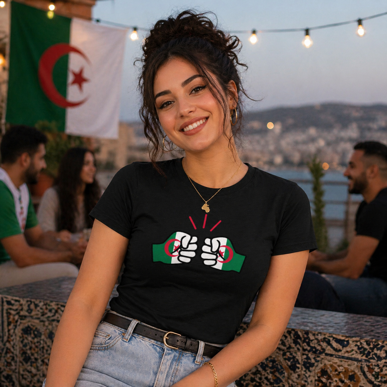 Woman wearing a black t-shirt with a We Run Tings Algerian theme, sitting outdoors with people and flags in the background.