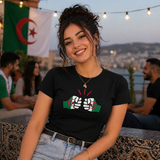 Woman wearing a black t-shirt with a We Run Tings Algerian theme, sitting outdoors with people and flags in the background.