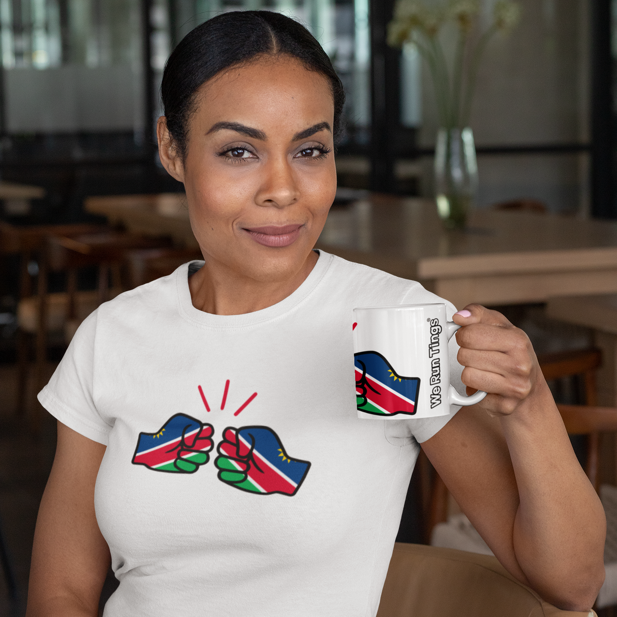 Woman holding a We Run Tings Namibia themed mug with a matching design t-shirt, sitting in a casual setting.