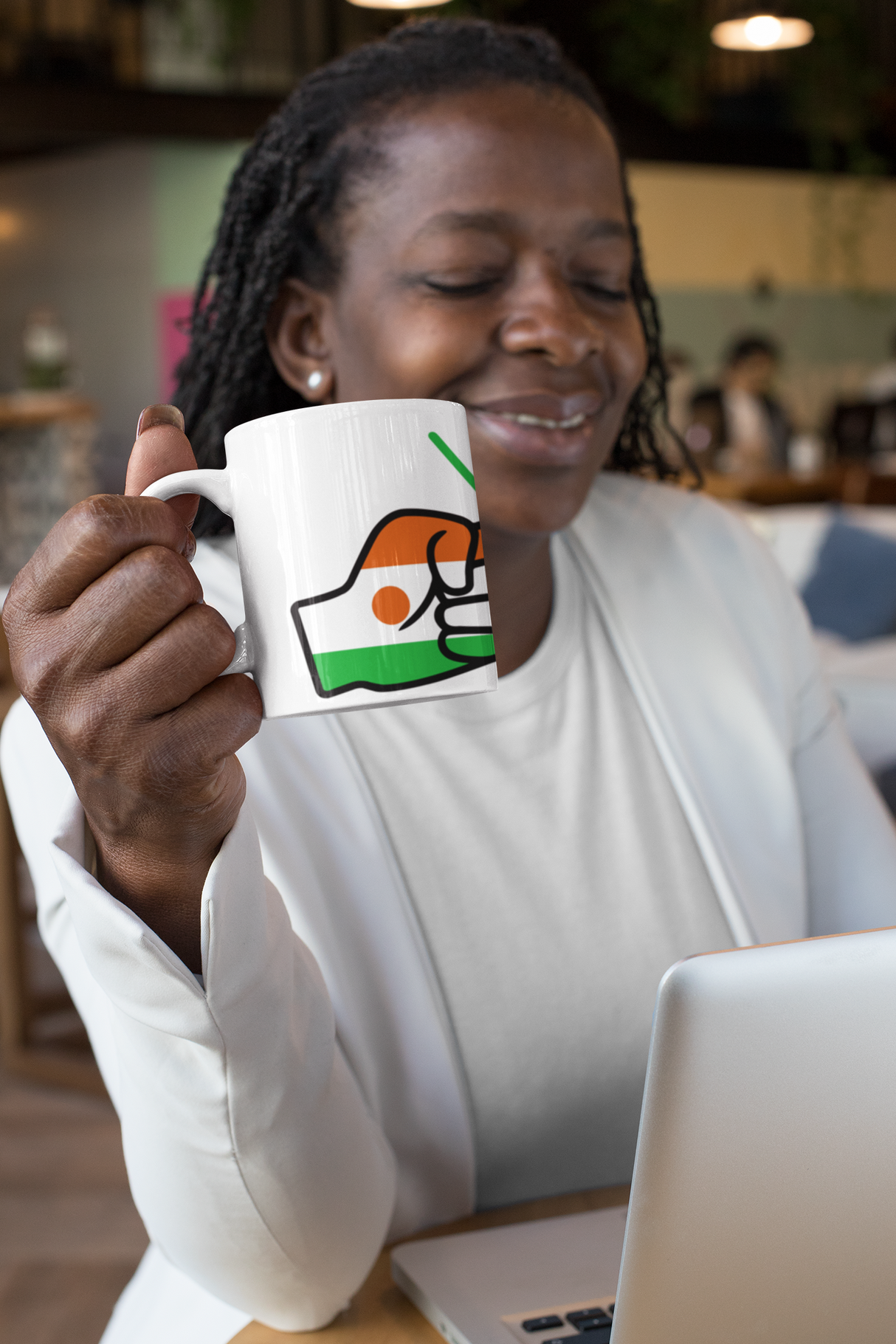 Black woman sitting at a table working on a computer holding a white ceramic We Run Tings Niger themed  coffee, tea cup, mug