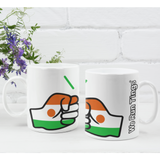 A pair of glossy white ceramic We Run Tings Niger tea, coffee mugs, cups with a graphic design of the brand and the colours of the flag of Niger. Side view with a white brick background.
