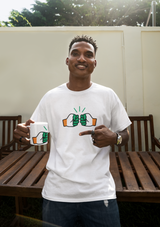 Man wearing a white Cote D'Ivoire t-shirt with a graphic design, holding a We Run Tings mug outdoors.