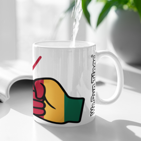 White ceramic We Run Tings Mali tea, coffee mug, cup with colourful design and text being filled with water, placed on a white surface with a plant in the background.
